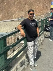 A man wearing sunglasess learning against a railing out doors